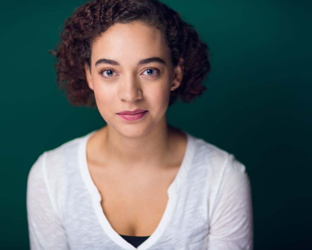 Headshot of Aislinn Brophy, a mixed-race Black and white person with short curly brown hair.
